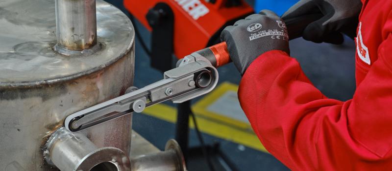 Bild på person som slipar en svetsad fog med bandfilmaskin